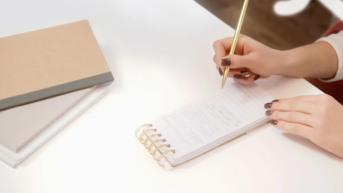 Handen die aantekeningen maken in een notitieboek op een wit bureau