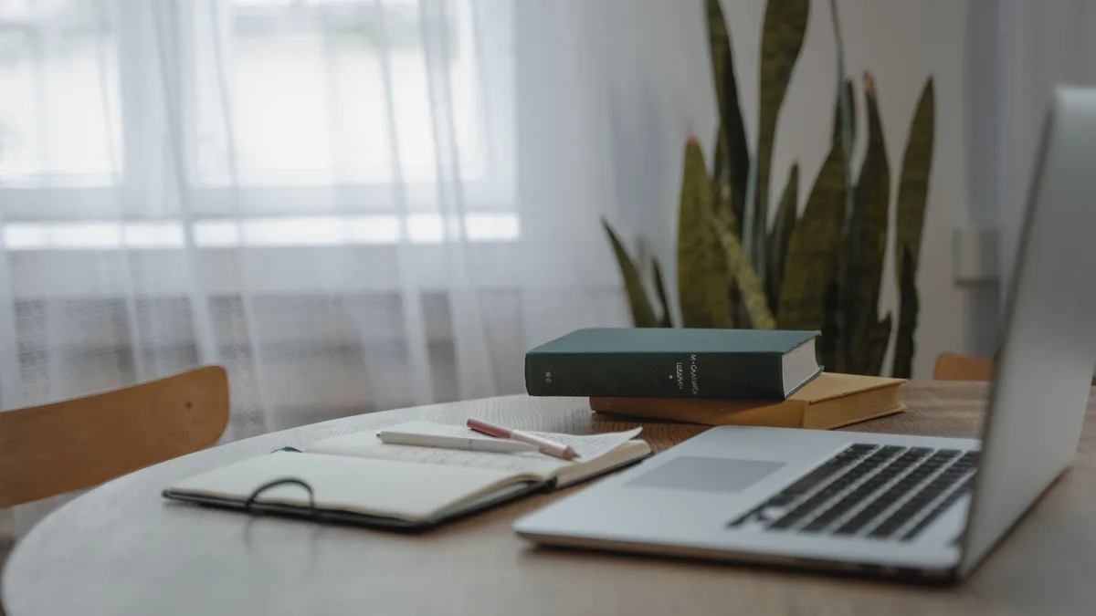 Quiet workspace with a laptop and an open notebook on a wooden table by the window