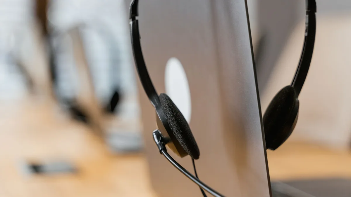 Zwarte headset die over de rand van een opengeklapte laptop hangt op een houten bureau, met een zachte onscherpe achtergrond